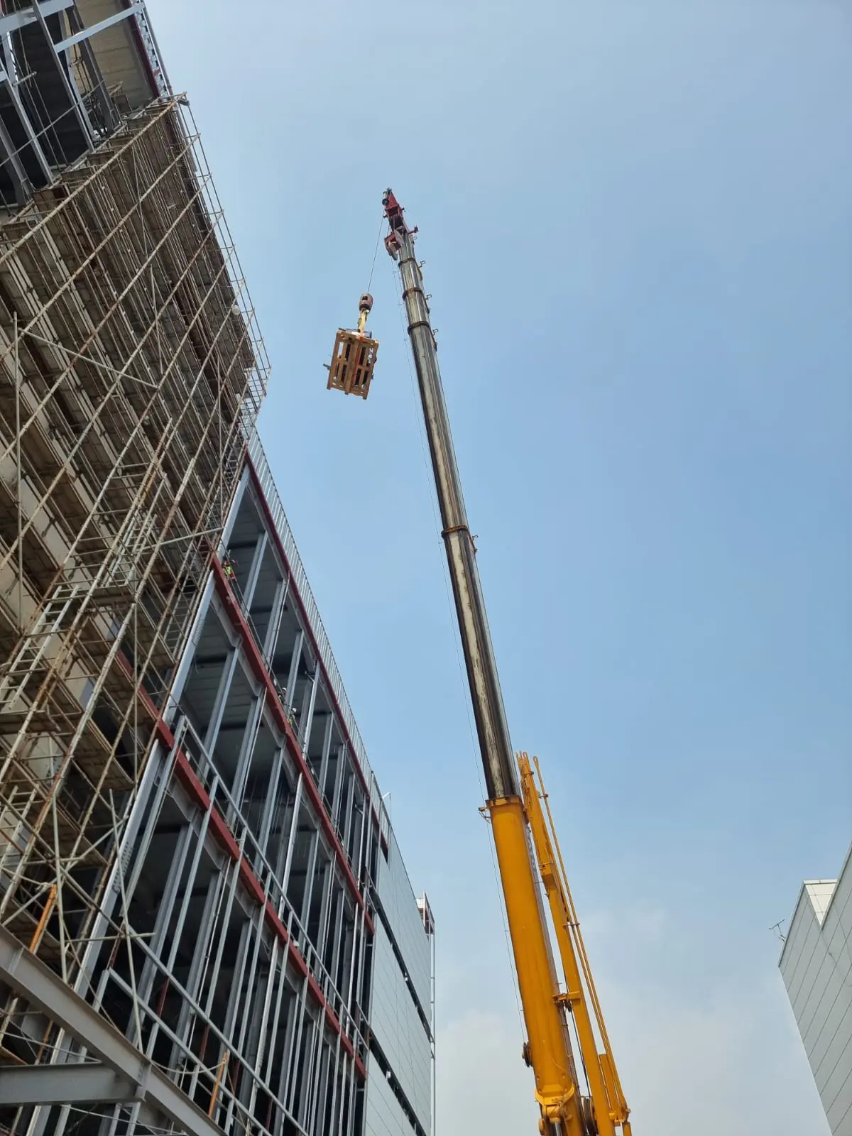 Crane hoisting a load beside a scaffolded steel-frame building on the PTJ Hyundai LG Battery site